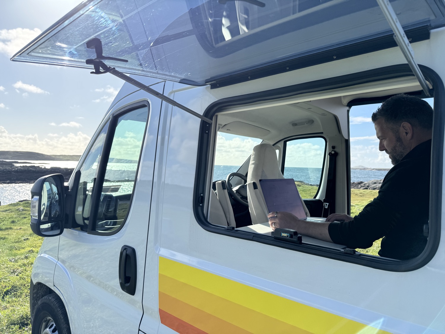 Nick working on a laptop inside a campervan parked beside the ocean in Galway