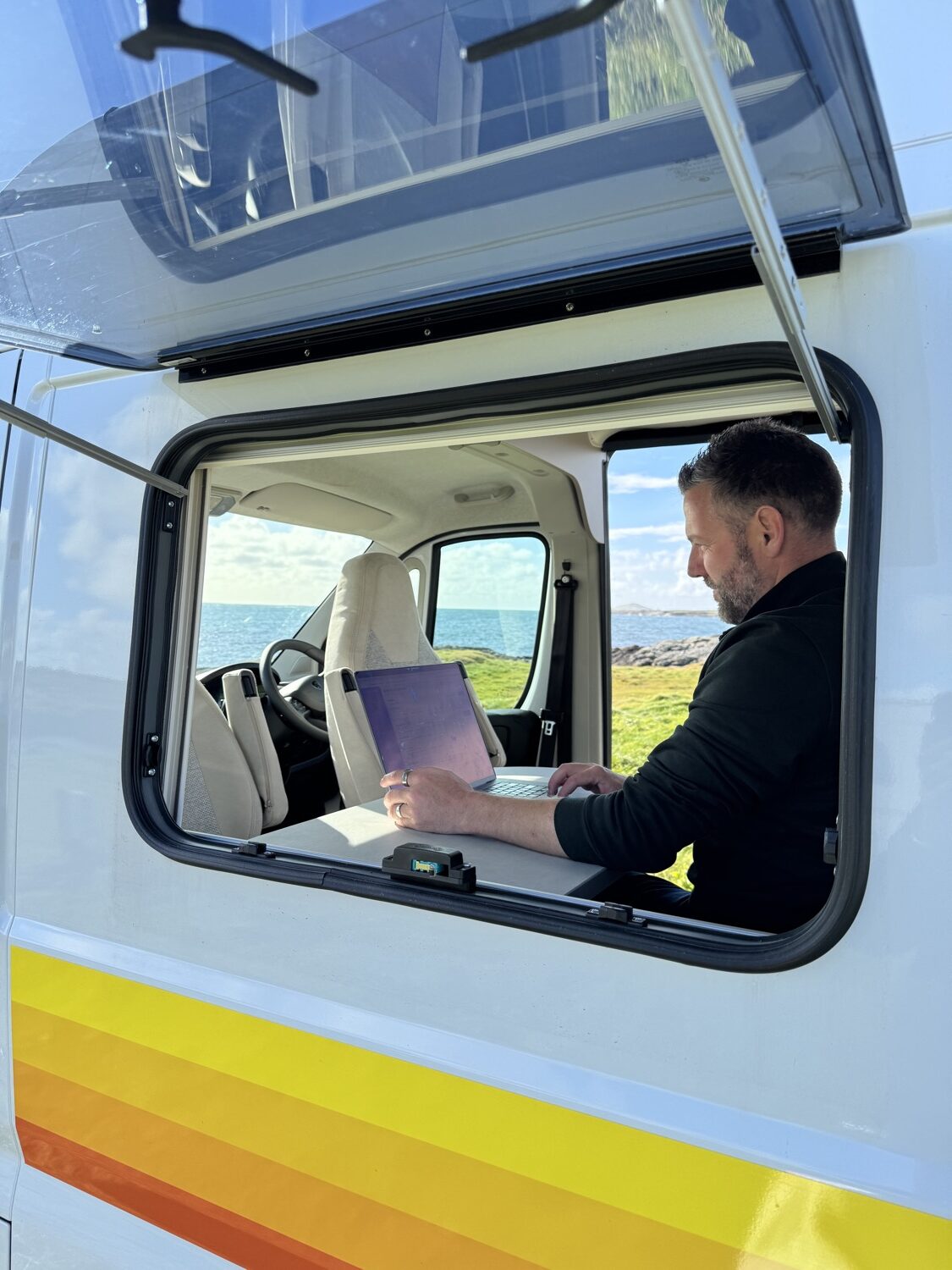 Nick working on a laptop inside a campervan with the ocean visible through the window